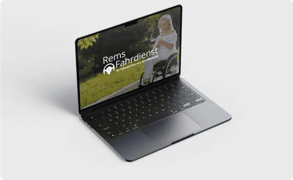A sleek laptop displays a smiling person in a wheelchair on the screen, with "Rems Fahrdienst" text overlay. The scene is set in a sunny park.